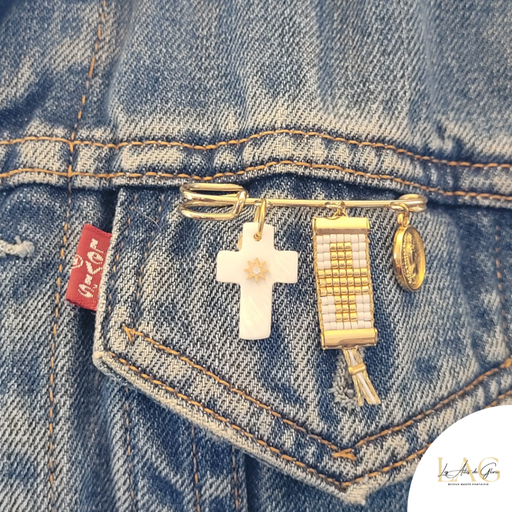 Gold-tone bracelet with multiple charms clipped to a blue denim jacket pocket: a cross pendant, a gold bead watch, and a small oval locket, with a red Levi's tag nearby.
