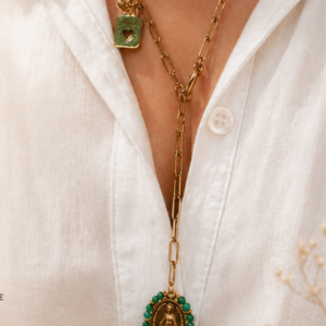 Gold multi-layered necklace with a green-beaded oval pendant featuring a religious figure, worn over a white blouse.