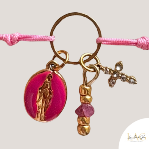 Charm bracelet with a pink oval religious medal, gold beaded pendant, and a tiny cross on a pink cord.