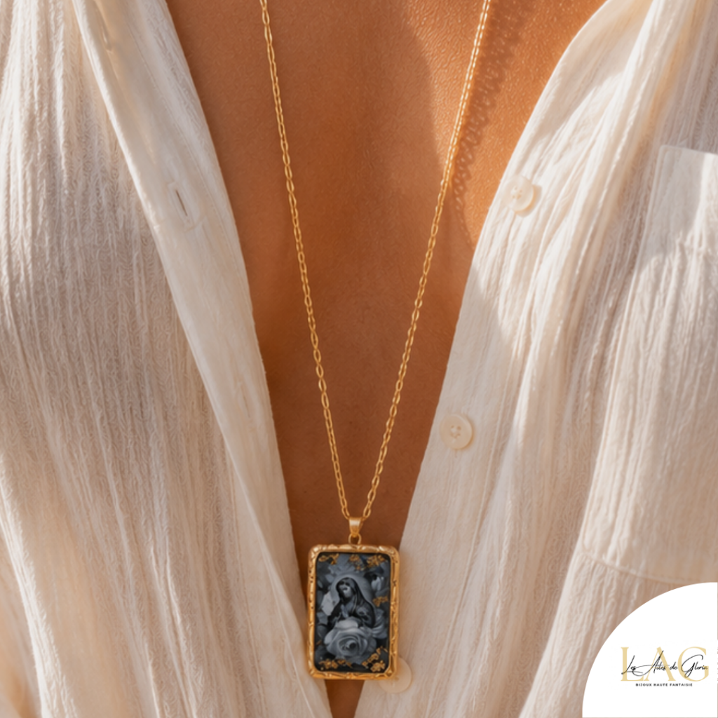 Gold chain necklace with a rectangular pendant showing a dark image framed in gold, worn over a sheer white blouse.