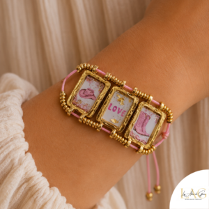 Gold-framed bracelet with three square tiles on a pink cord; center tile says LOVE with pink accents.
